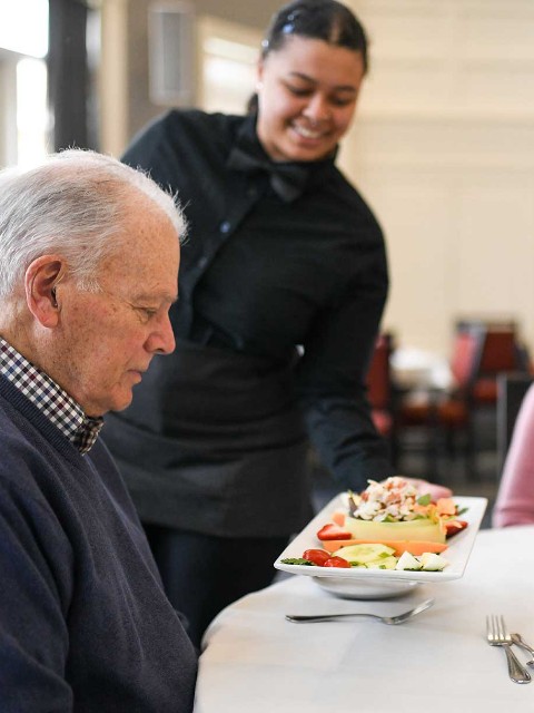 Server bringing dish to senior man