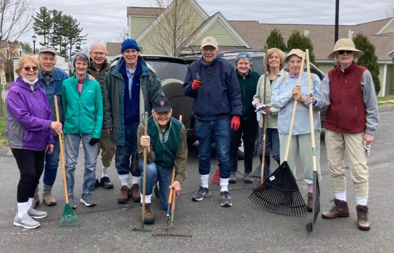 A group of residents from The Commons in Lincoln’s Garden and Landscape Committee stand together outdoors holding rakes and gardening tools during a spring clean-up.