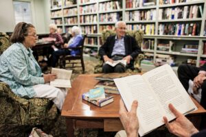Residents gather in a library at The Commons in Lincoln, reading books and participating in a book discussion surrounded by floor-to-ceiling bookshelves.