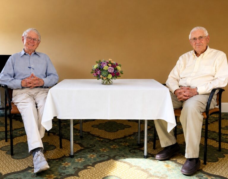 Dr. Timothy Johnson and Ted Koppel seated on either side of a white-covered table with a floral arrangement during a special event at The Commons in Lincoln.
